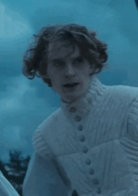 a man with curly hair is wearing a white sweater and a white vest .