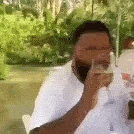 a man in a white shirt is sitting at a table drinking a glass of wine .