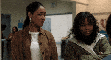 two women stand next to each other in a hallway with an exit sign above them