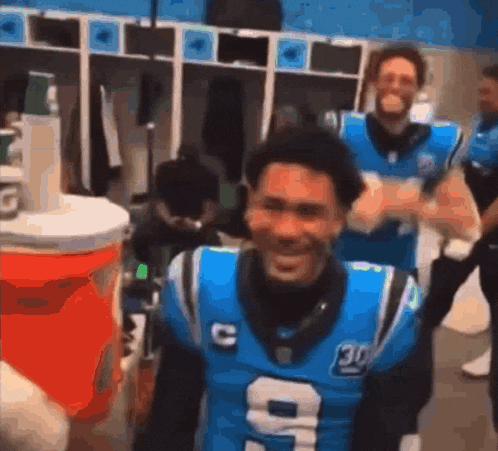 a man in a carolina panthers jersey is standing in a locker room .