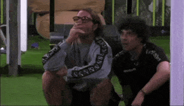 a man wearing glasses is sitting next to another man wearing a black shirt that says givova on it .