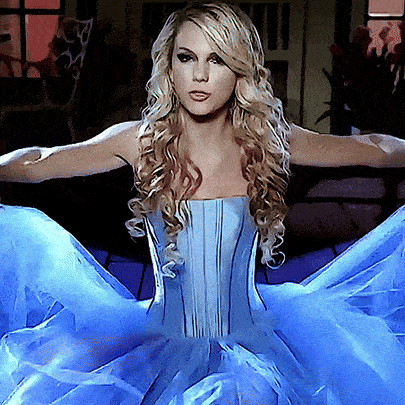 a blonde woman in a blue dress with her arms outstretched looks at the camera