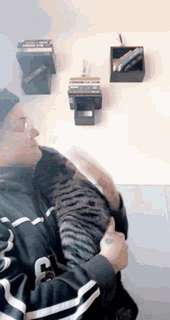 a man is holding a cat in his arms in front of a bookshelf .