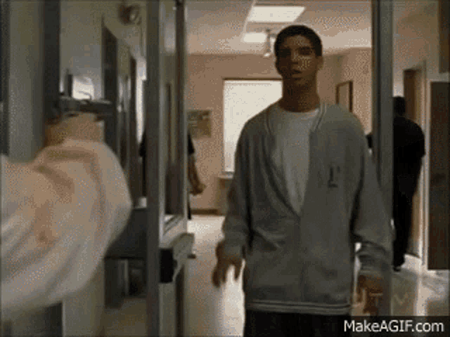 a man in a grey jacket is standing in a hallway in front of a door .