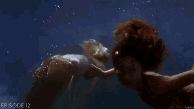 a mermaid is swimming in the ocean and touching another mermaid 's tail
