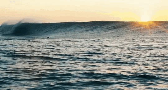 a surfer is riding a wave in the ocean with the sun setting behind him