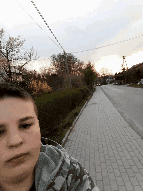 a boy in a camo hoodie stands on a sidewalk