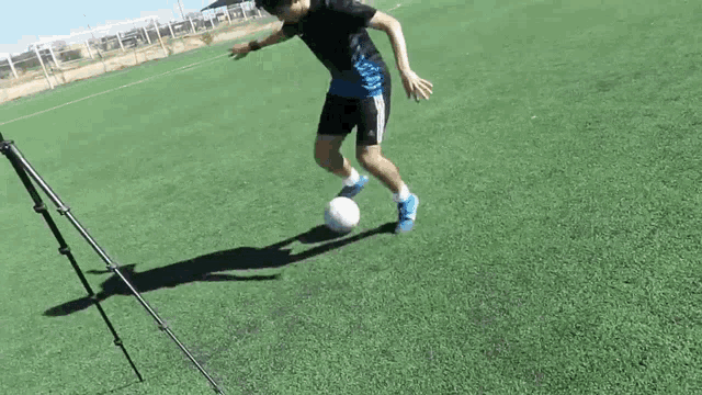 a man in a black shirt and blue shorts is kicking a soccer ball