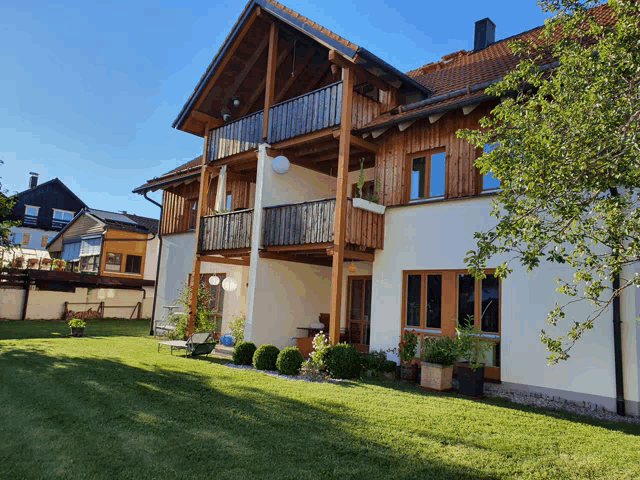 a white house with a wooden balcony sits in a lush green yard