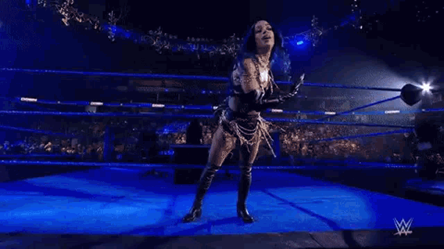 a female wrestler is standing in a wrestling ring holding a sword .