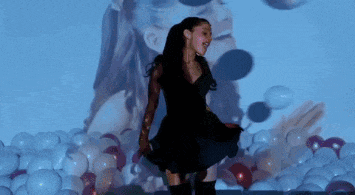 a woman in a black dress is dancing in front of a projector screen with balloons projected on it .