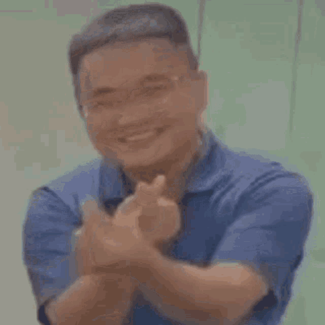 a man in a blue shirt is smiling and giving a heart with his finger .