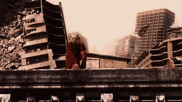 a man in a red jacket is kneeling on a ledge overlooking a city