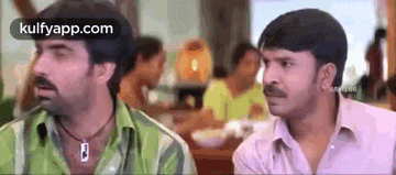 two men are sitting next to each other in a restaurant and looking at something .
