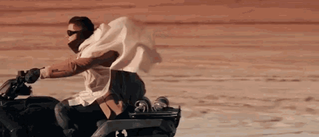 a man wearing sunglasses and a white cape is riding a motorcycle .