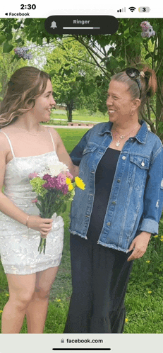 a woman in a denim jacket stands next to a woman in a white dress holding flowers