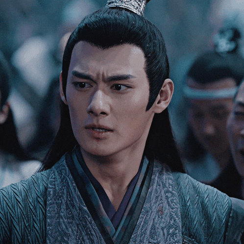 a man with long black hair and a crown on his head looks at the camera