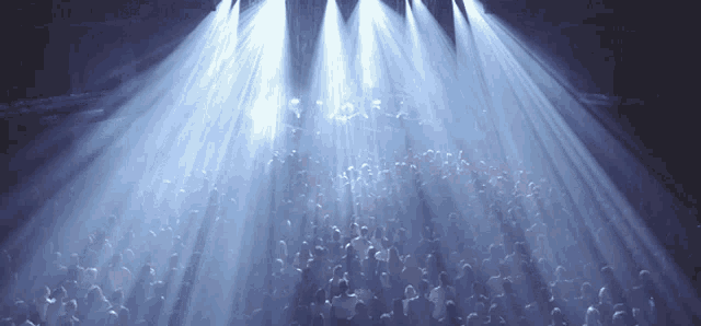 a crowd of people are gathered in a dark room under a spotlight