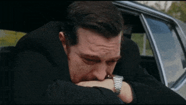 a man in a black suit is sitting in the back seat of a car .