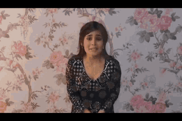 a woman standing in front of a floral wallpaper