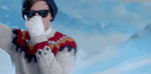 a man wearing a sweater , sunglasses , and gloves is standing in the snow .