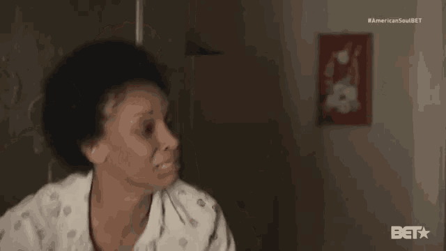 a woman in a polka dot shirt is sitting in a dark room with a bet logo in the corner
