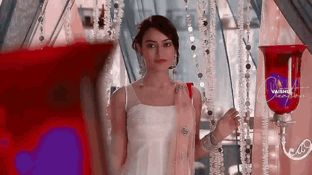 a woman in a white dress is standing in front of a red vase