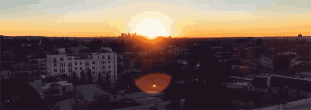 the sun is setting over a city with a few buildings in the foreground