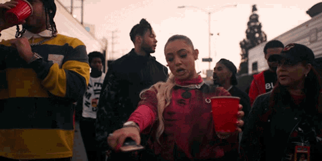 a group of people are walking down a street and one of them is holding a red cup