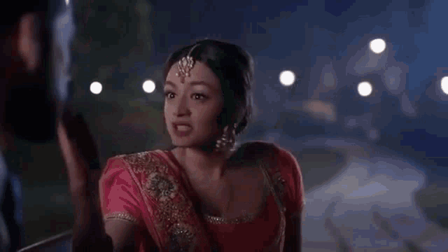 a woman in a red sari is reaching out to a man in a dark room .