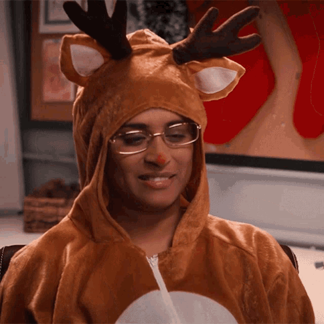 a woman wearing glasses and a reindeer costume has a red nose