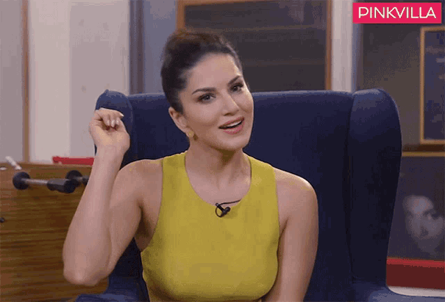 a woman in a yellow tank top sits in a blue chair with a pinkvilla logo in the background