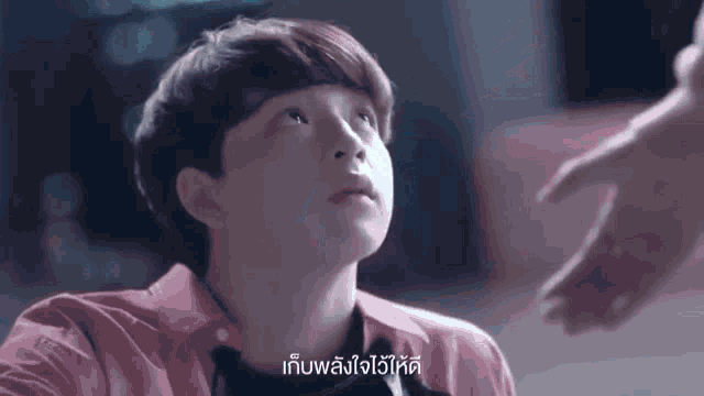 a young boy in a pink shirt is looking up at a hand .