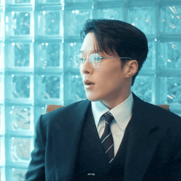 a man wearing glasses and a suit is sitting in front of a brick wall