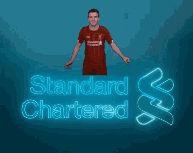 a man in a red shirt is standing in front of a blue sign that says standard chartered