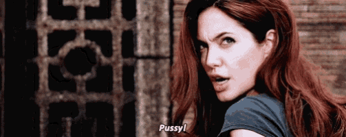 a woman with red hair is standing in front of a brick wall and says pussy .