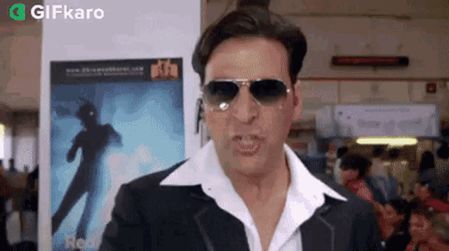 a man wearing sunglasses and a white shirt is standing in front of a poster that says gifkaro