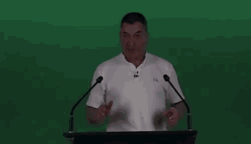 a man in a white shirt is standing at a podium with his arms outstretched .