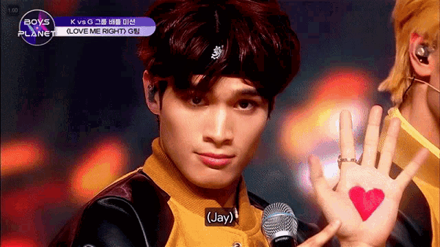 a young man holds up his hand with a heart painted on it and says " jay "