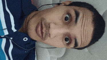 a man wearing a blue and white striped shirt and ear buds looks surprised