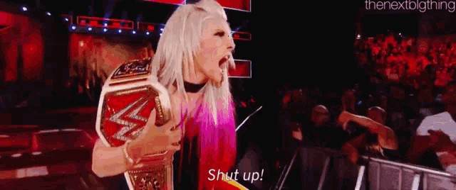 a woman is holding a wrestling championship belt and screaming at the crowd .