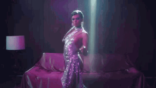 a woman in a sequined dress is dancing in a dark room with purple lights .