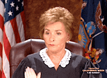 a female judge sitting in front of an american flag with california week written on her shirt