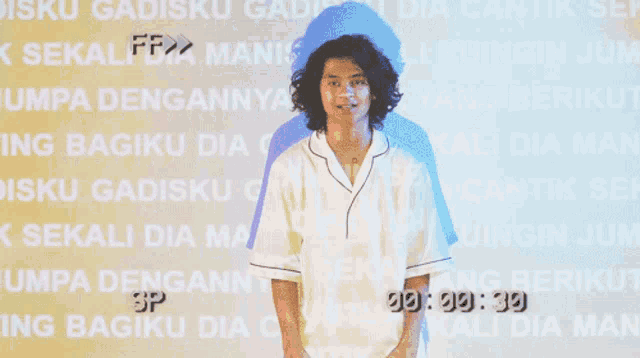 a man in a white shirt is standing in front of a wall that says ' disku dia cantik '