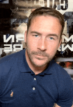 a man wearing a blue polo shirt stands in front of a poster that says ' a ' on it