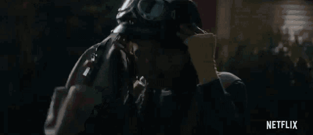 a man in a helmet and goggles is kissing another man in a dark room .