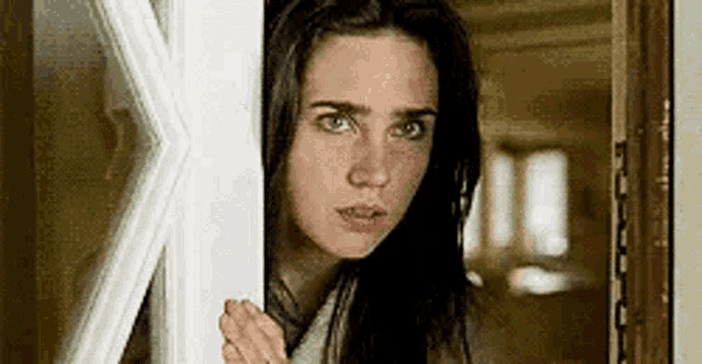 a woman is peeking out of a door and looking at the camera .