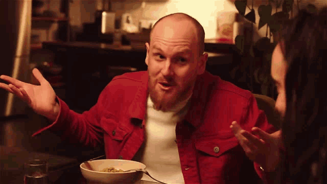 a man in a red jacket is sitting at a table with a bowl of food in front of him
