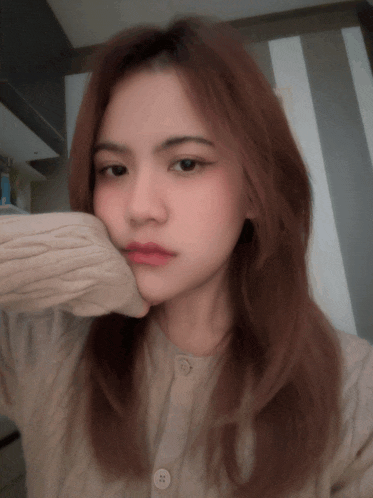 a woman wearing a tan sweater with buttons on the front is taking a selfie