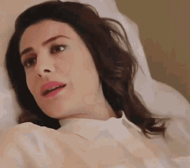 a woman in a white shirt and pink lipstick is laying in a hospital bed .